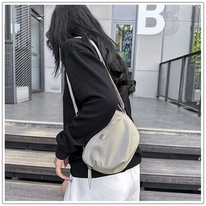 Close-up of beige crescent crossbody bag featuring metal logo and adjustable strap