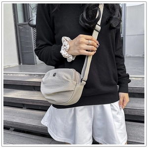 Detail of light beige crescent nylon bag with pleats and adjustable strap on a model