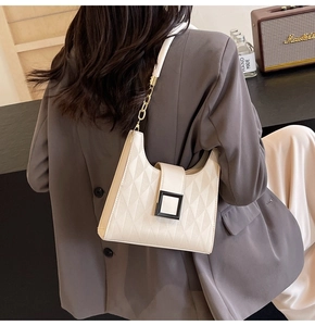 Close-up of beige quilted shoulder bag with metal buckle and chain strap on a model
