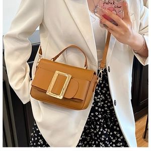 Side view of a brown leather handbag with a large gold buckle on a stylish woman