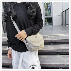 Adjustable wide strap on beige nylon crossbody bag shown in outdoor setting