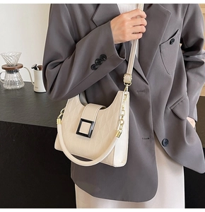 Quilted beige bucket bag with chain strap and black clasp shown on model in a cafe