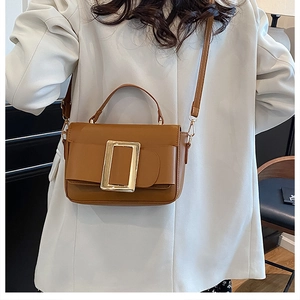 Detail of a brown small square bag featuring a prominent gold metal buckle on a white blazer
