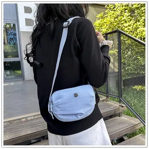 Outdoor view of a light blue nylon crossbody bag with dual zippers and adjustable strap