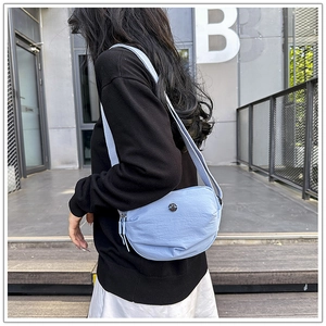 Outdoor close-up of light blue nylon crossbody bag with double zippers and wide strap