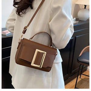 Detail of a brown leather crossbody bag with a large gold metal buckle on a shoulder