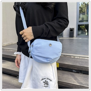 Detail of light blue nylon crossbody bag with metal logo and adjustable strap