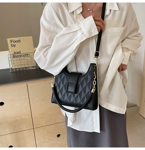 Detail of black quilted bucket bag featuring a gold chain strap and square metal buckle