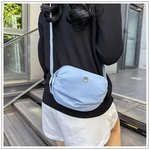 Close-up of a light blue nylon crescent crossbody bag with metallic logo and wide strap