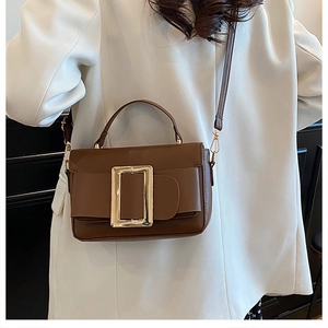 Detail of a brown vintage square handbag with a large gold buckle on a white blazer