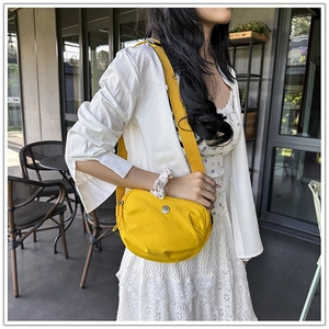 Detail of a bright yellow nylon crossbody bag with an adjustable strap and metal logo
