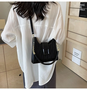 Detailed side view of black quilted bucket bag with irregular curved opening and metal chain