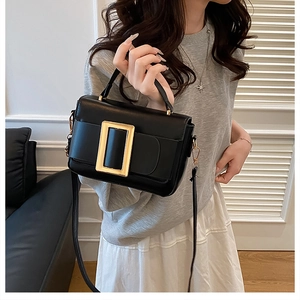 Close-up of black leather handbag featuring a signature polished gold rectangular buckle