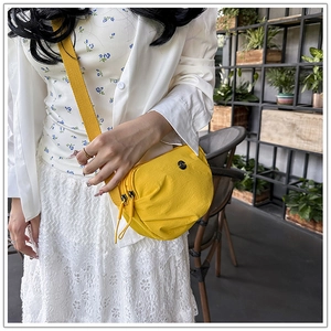 Detail of yellow nylon crossbody bag featuring dual zippers and adjustable wide strap