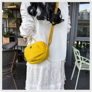 Detail of a bright yellow nylon crossbody bag featuring a half-moon pleated fashion design