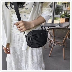 Detail view of a black nylon round crossbody bag with double zippers and adjustable strap
