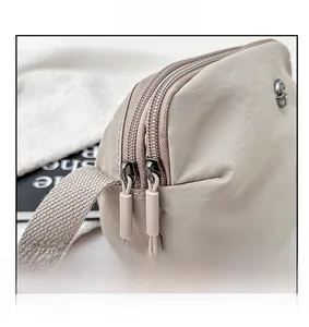 Detail of smooth double zippers and round metal logo on beige nylon crossbody bag