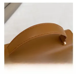 Close-up of dual-stitched leather handle and metal buckle on caramel crossbody bag