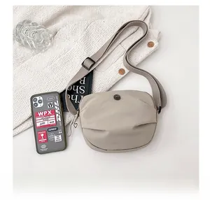 Flat lay of a lightweight beige nylon crossbody bag with adjustable wide strap and metal logo
