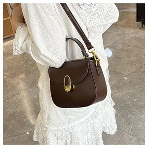 Detail view of a brown semi-circle crossbody bag with gold U-shaped lock on a model