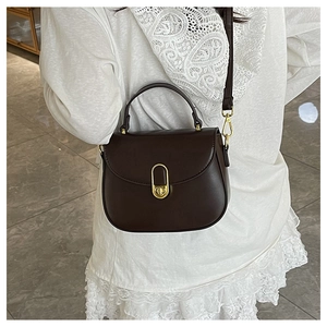 Detail of dark brown leather crossbody bag with elegant gold oval twist lock and top handle