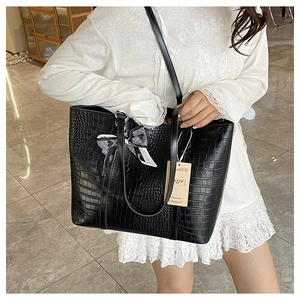 Detail of black crocodile pattern tote bag featuring a bow charm and long shoulder strap