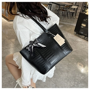 Detail of black crocodile texture tote bag with a polka dot bow scarf and hanging tag