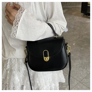 Detail of black leather saddle bag featuring a textured gold clasp and adjustable strap