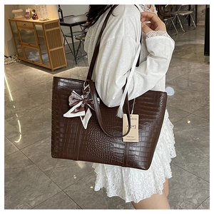Detail of crocodile embossed dark brown tote bag with decorative patterned silk scarf