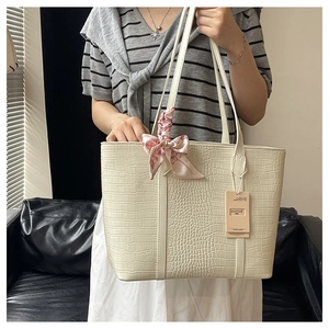 Detail of cream crocodile embossed tote bag with floral scarf accessory on a model