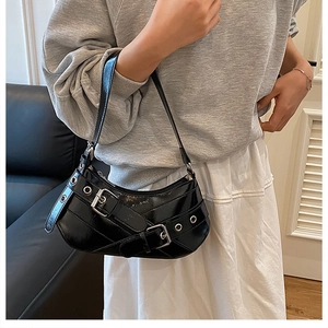 Détail du sac croissant en cuir noir brillant avec des œillets argentés et des accents punk