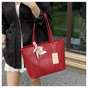 Détail d'un sac cabas rouge à motif crocodile avec un foulard floral décoratif au manche