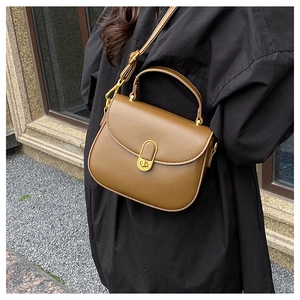 Chic brown leather shoulder bag with gold metal clasp on a black coat outfit