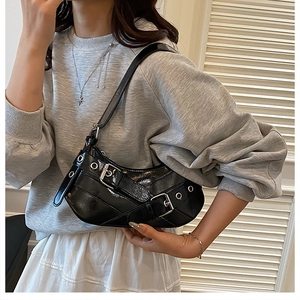 Close-up of black glossy patent leather shoulder bag with metal grommets and buckles