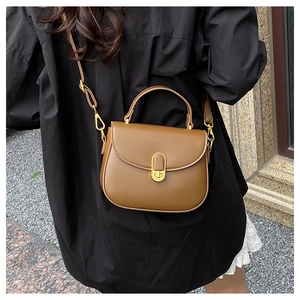 Brown vintage saddle bag with gold oval lock worn by a model in casual chic attire