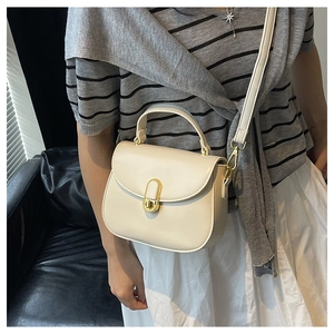 Detail of a creamy white crossbody bag featuring a golden U-shaped clasp and metal hardware