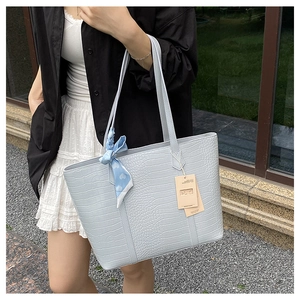 Macro shot of light blue croc-embossed tote bag featuring a heart print silk scarf detail