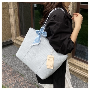 Detail of light blue crocodile-embossed tote bag with elegant silk scarf accent