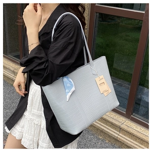 Détail d'un sac cabas bleu clair à motif crocodile avec foulard en soie sur l'anse
