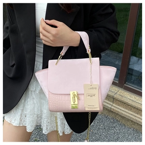 Detail of light pink wing bag with crocodile texture and metal chain strap held by model