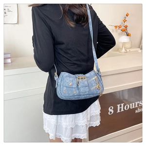 Detail showing blue denim crossbody bag with floral patterns and star charms on model