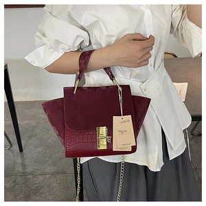 Detail of burgundy crocodile-embossed and matte leather handbag with gold clasp lock