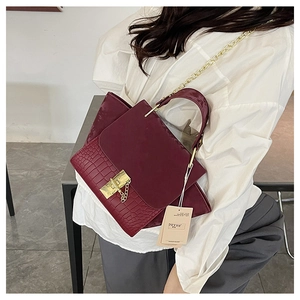 Detail of burgundy crocodile-embossed handbag with gold clasp and chain shoulder strap