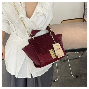 Detail of burgundy wing bag featuring crocodile texture and suede splicing with gold buckle
