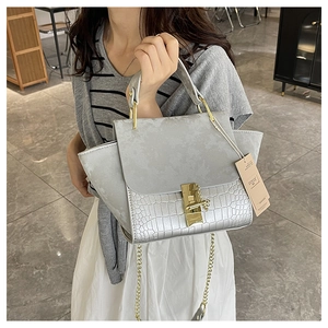 Detail of silver crocodile pattern patchwork handbag with gold metal handle and chain