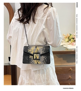 Detail of snake pattern crossbody bag with chain strap on a white dress