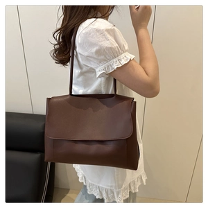 Deep brown PU leather tote bag with long shoulder strap shown in a minimal setting