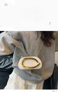 Macro shot of white leather mini bag featuring gold C-shaped buckle and metal chain strap