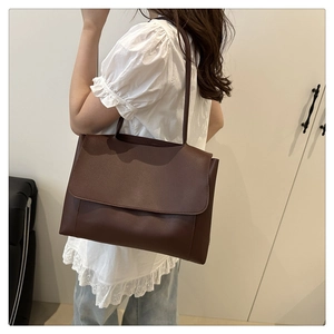 Detailed side view of a large dark brown PU leather tote bag worn by a model in a room