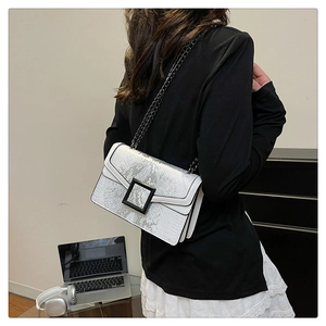 Detailed view of snake-print crossbody bag with metal chain strap on model in white dress